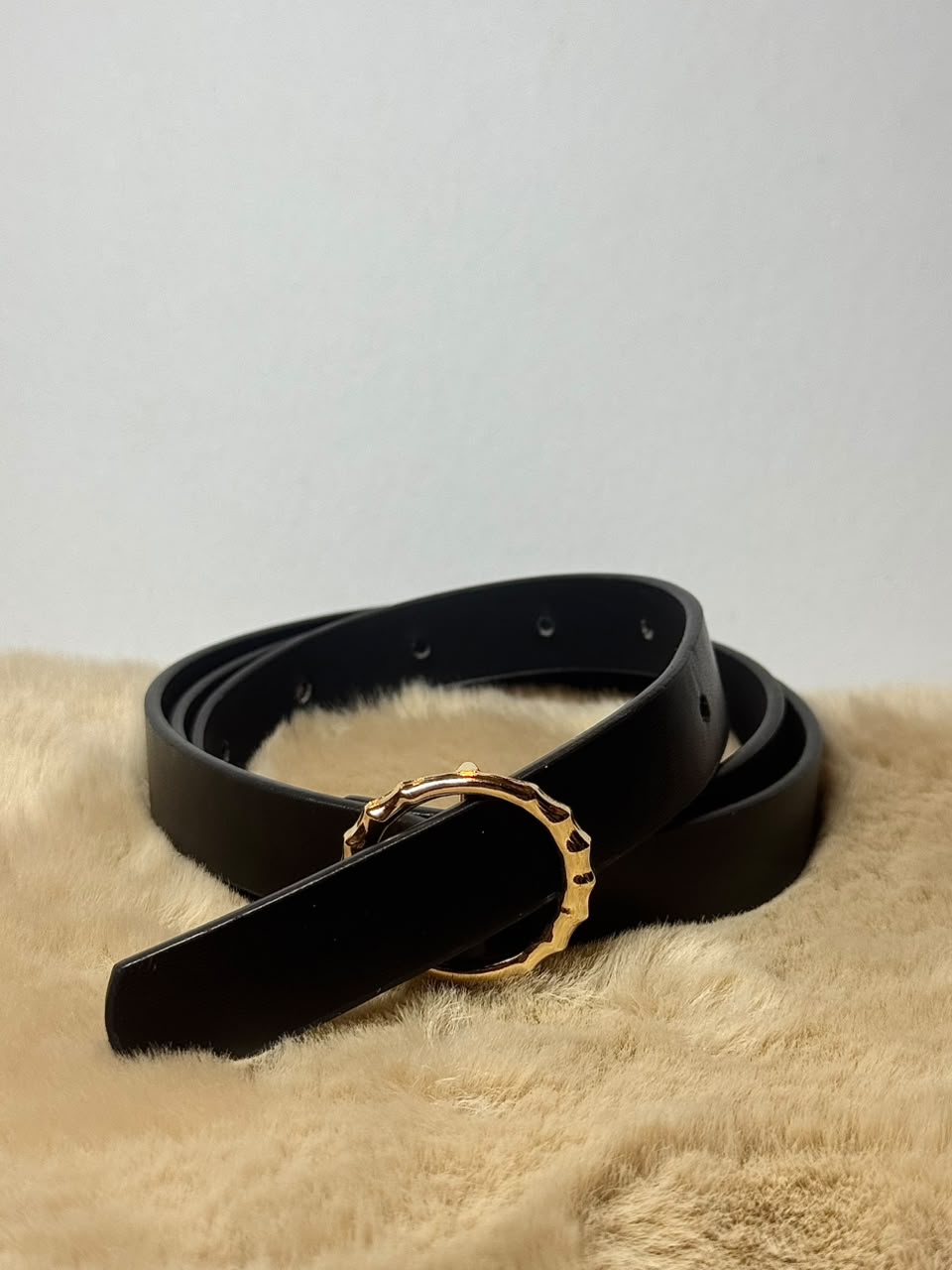 Cinturón negro delgado con hebilla circular dorada texturizada